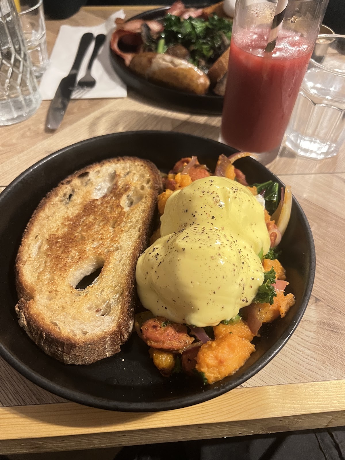 Eggs benedict with hollandaise on sweet potato and greens with toasted sourdough, beside a red smoothie