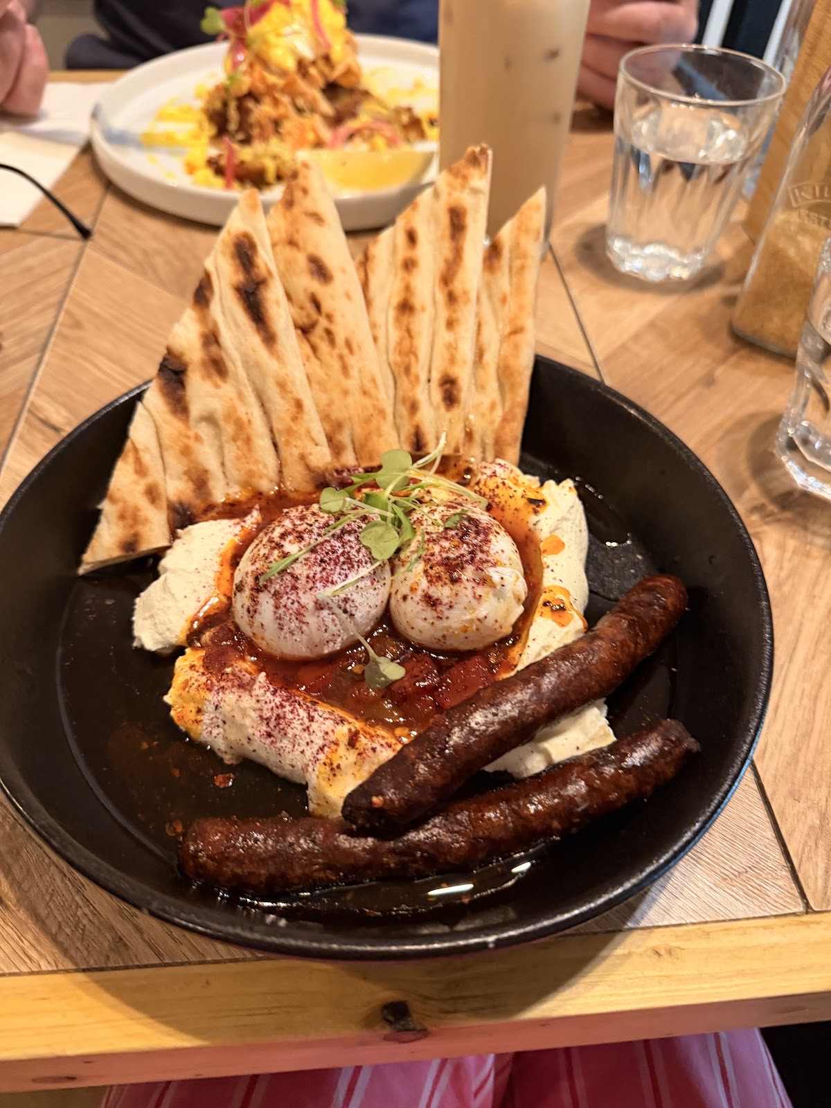 A pan of shakshuka-style baked eggs with sausages and toasted flatbread wedges