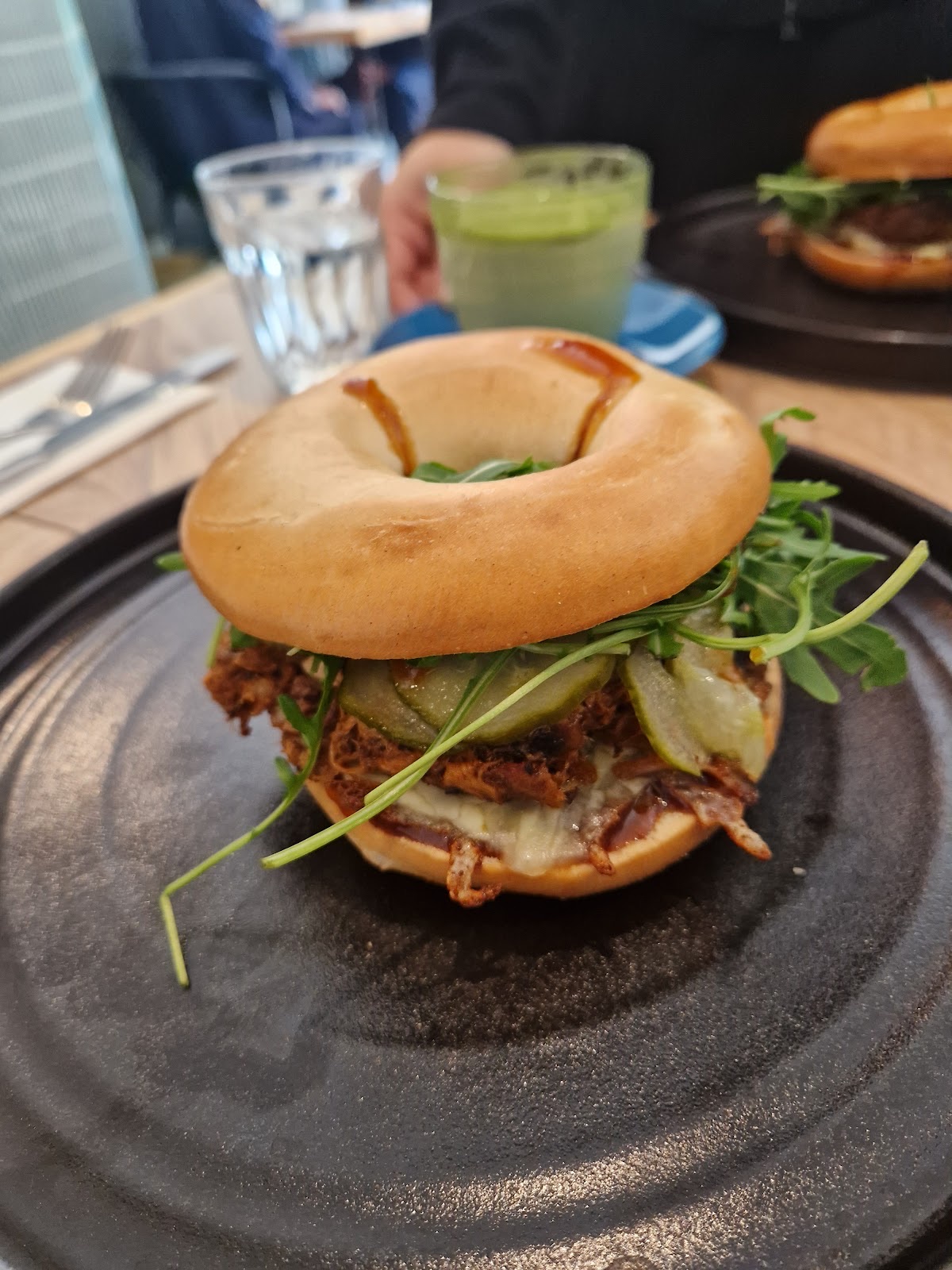 A filled bagel with pea shoots on a black plate