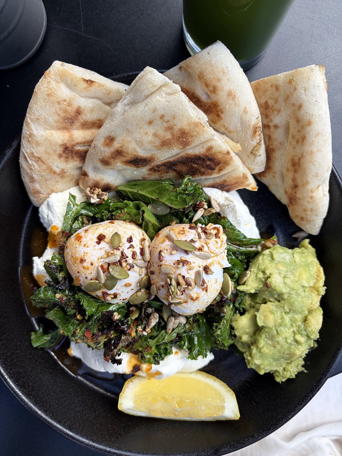 Poached eggs on greens with guacamole, lemon and toasted flatbread wedges